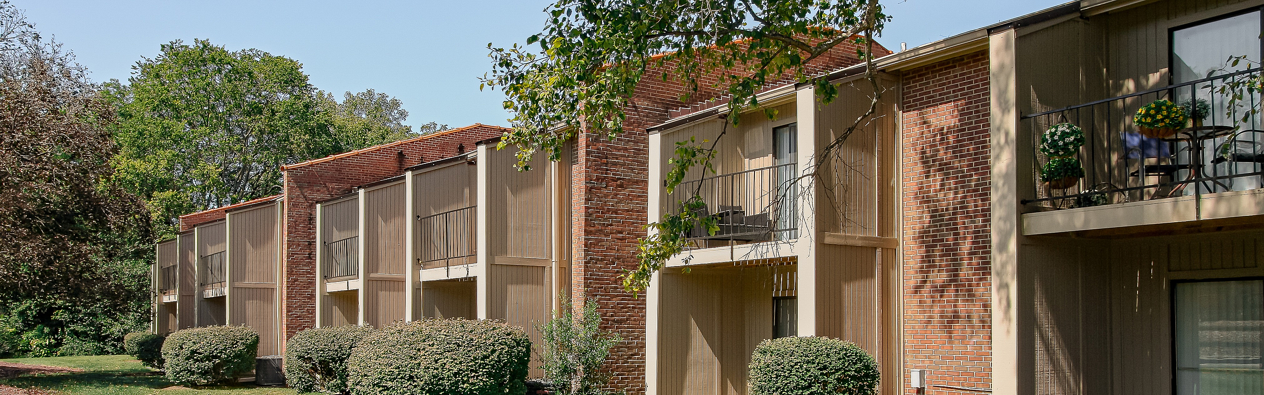 Charming brick apartment building with private balconies and lush greenery, ideal for relaxation.