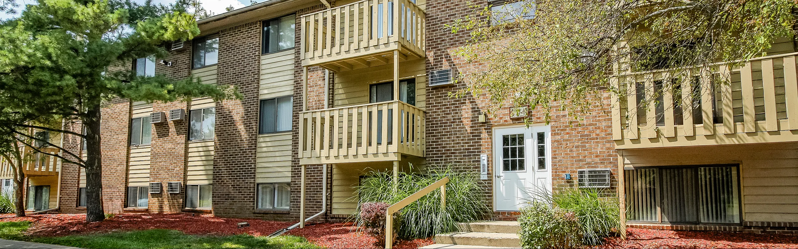 Charming brick apartment building with sunlit balconies and lush greenery, offering an inviting and serene living environment.