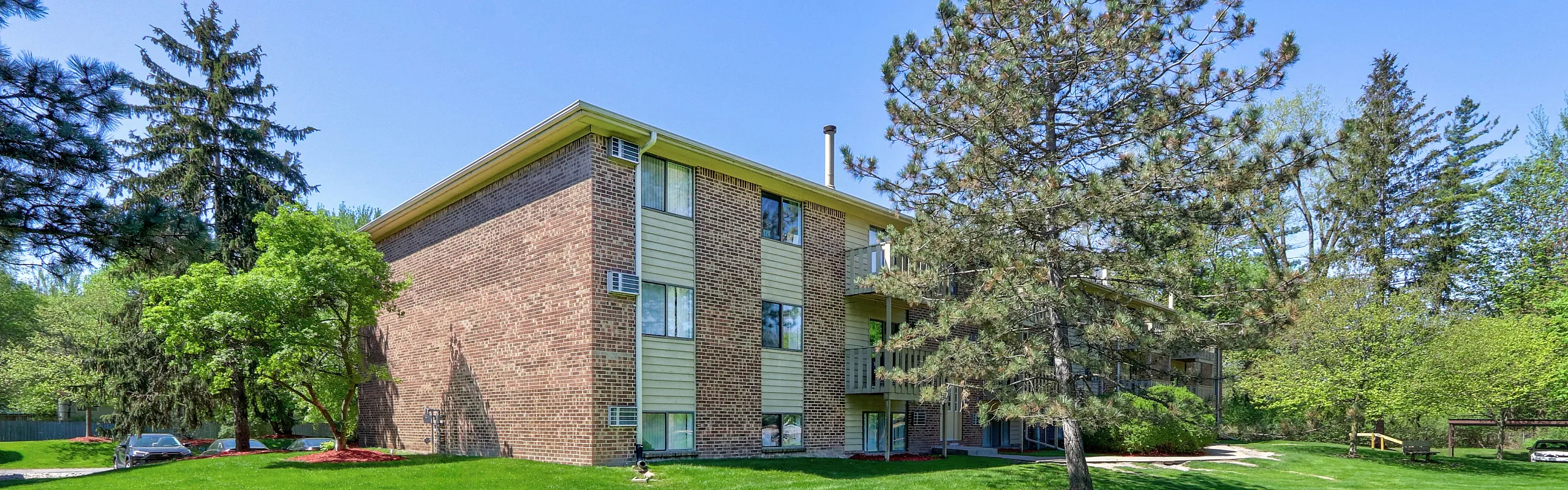 Charming brick apartment complex surrounded by lush greenery and mature trees, offering serene living.