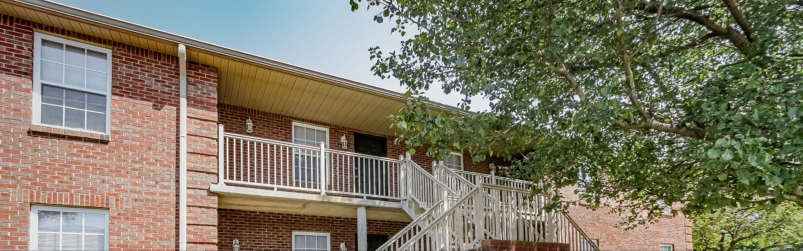 Charming brick apartment exterior with inviting balcony surrounded by lush greenery.
