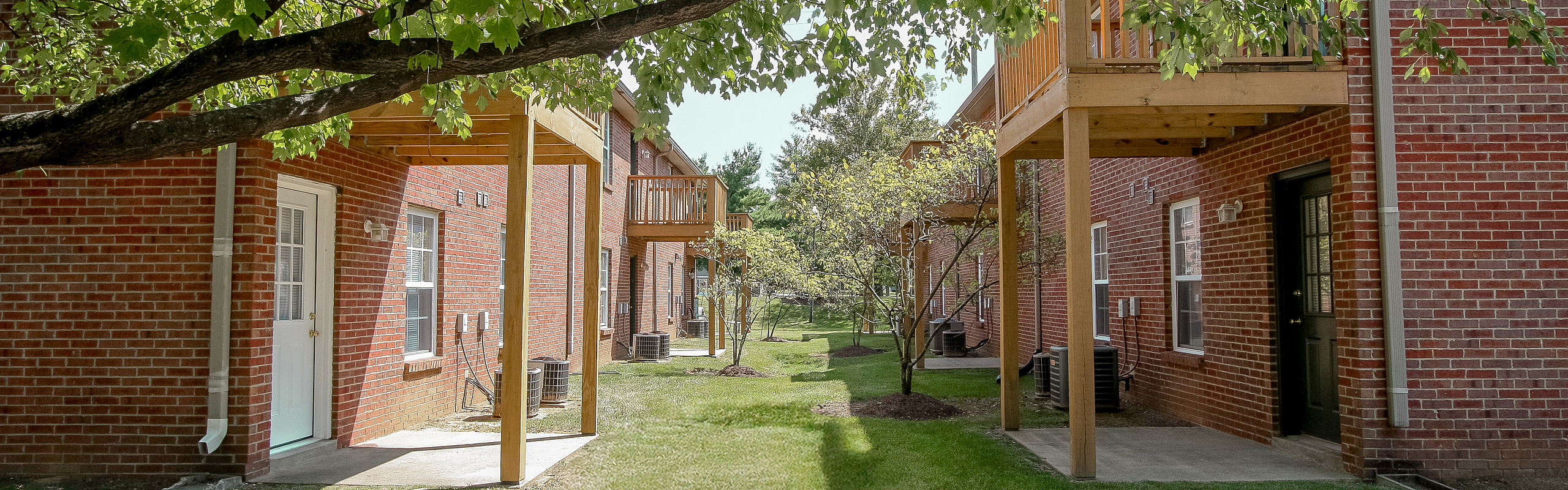 Charming brick apartment exterior with inviting balconies and lush green surroundings, perfect for relaxed living.