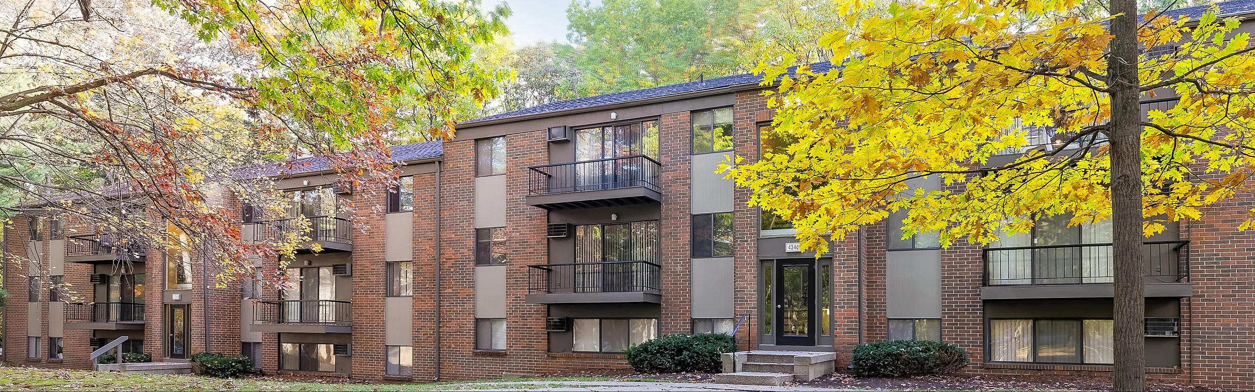 Charming brick apartment building surrounded by lush autumn foliage, featuring inviting balconies and large windows for ample natural light.
