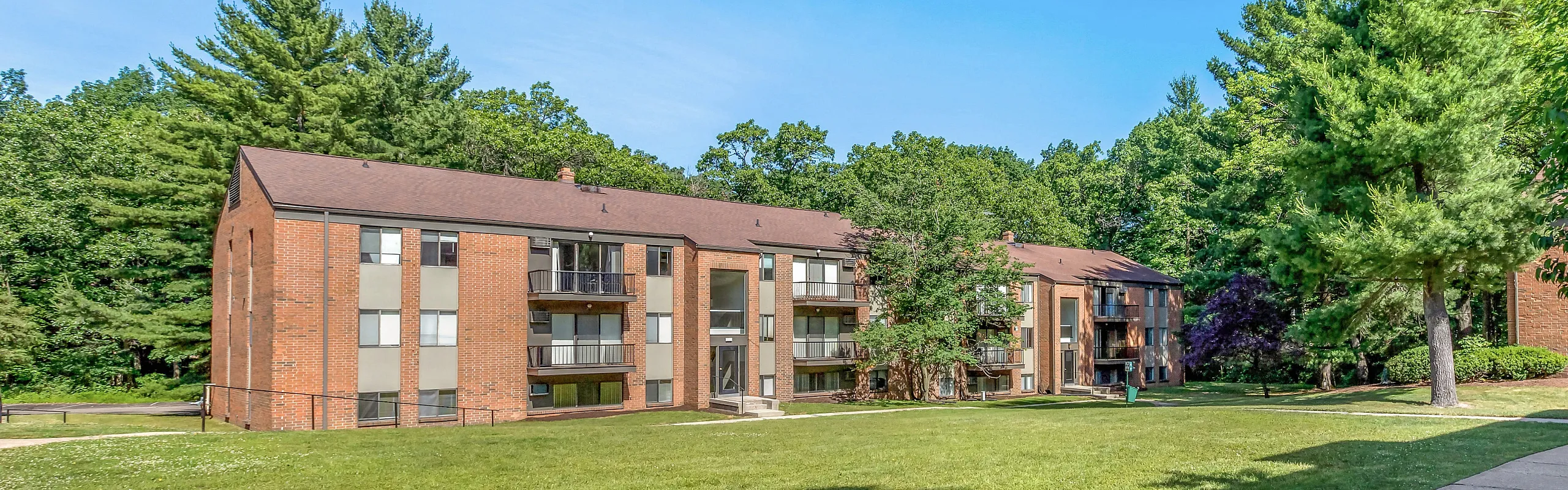 Charming brick apartment complex surrounded by lush greenery, offering serene living in a vibrant community setting.