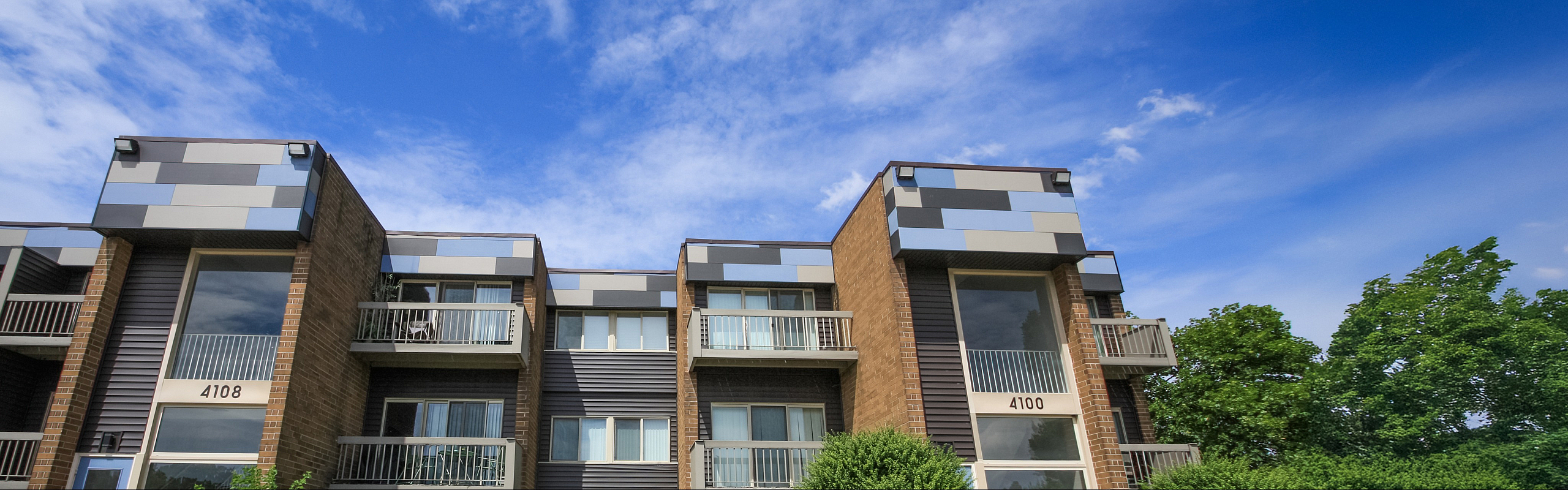 Modern apartment building with stylish exterior design, featuring bold geometric patterns and private balconies set against a bright blue sky.