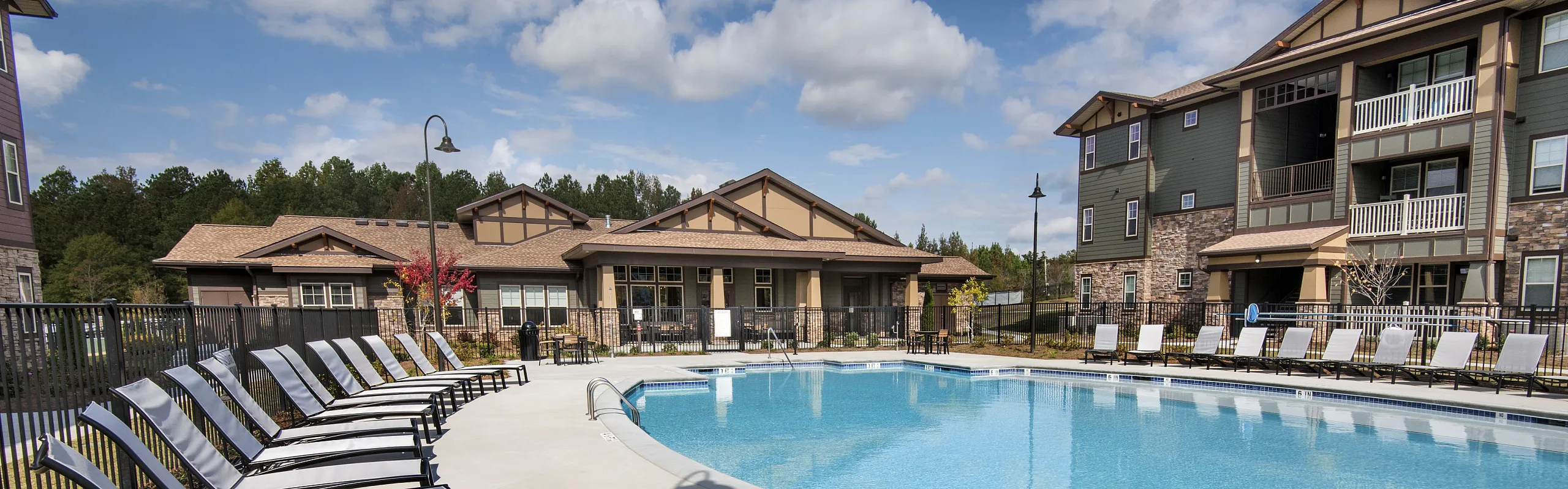 Luxurious apartment complex with a sparkling outdoor pool, elegant loungers, and modern architecture under a clear sky.