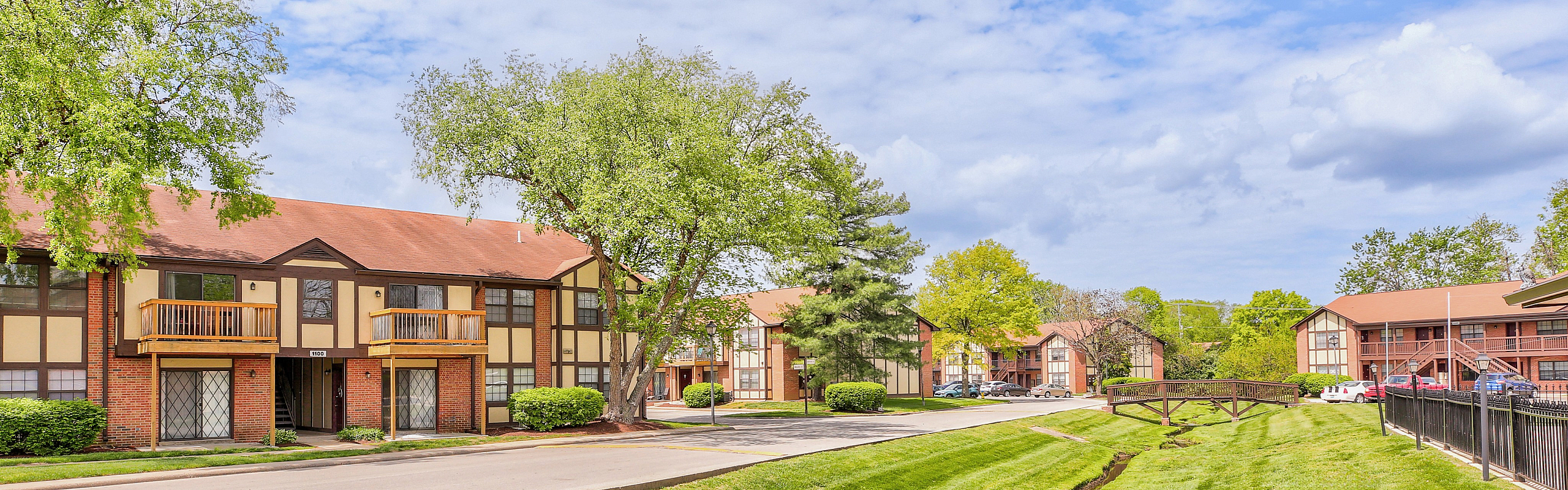 Charming apartment complex with Tudor-style architecture, lush landscaping, and spacious balconies for a serene living experience.
