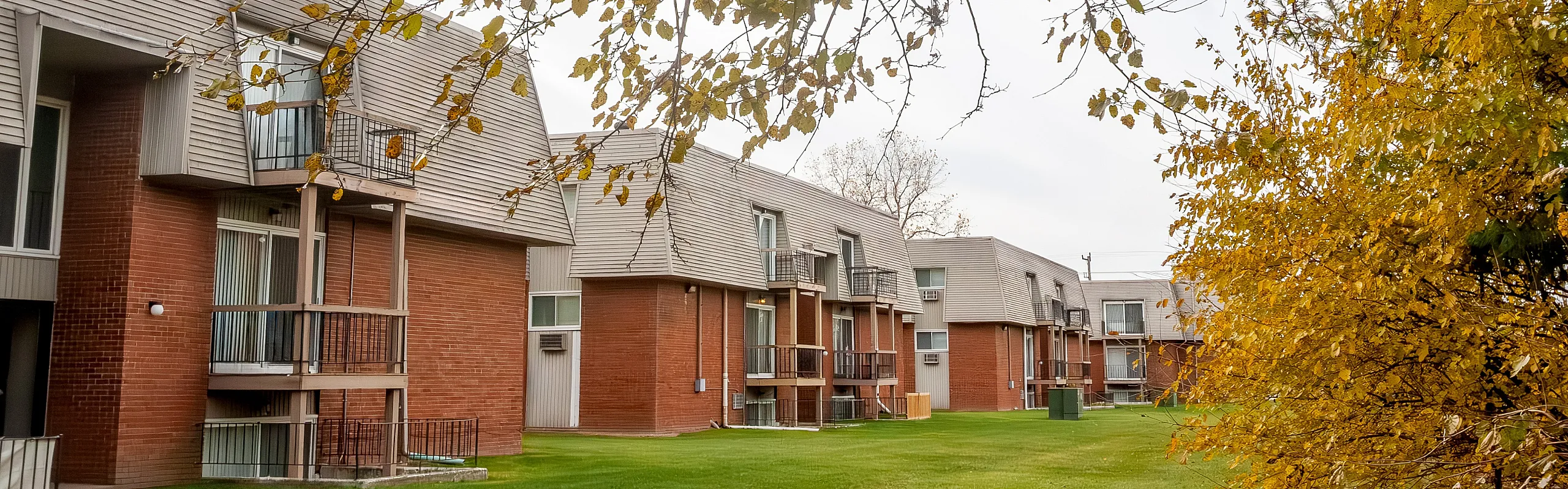 Charming apartment buildings with unique architectural design, surrounded by vibrant autumn foliage and lush green lawns.