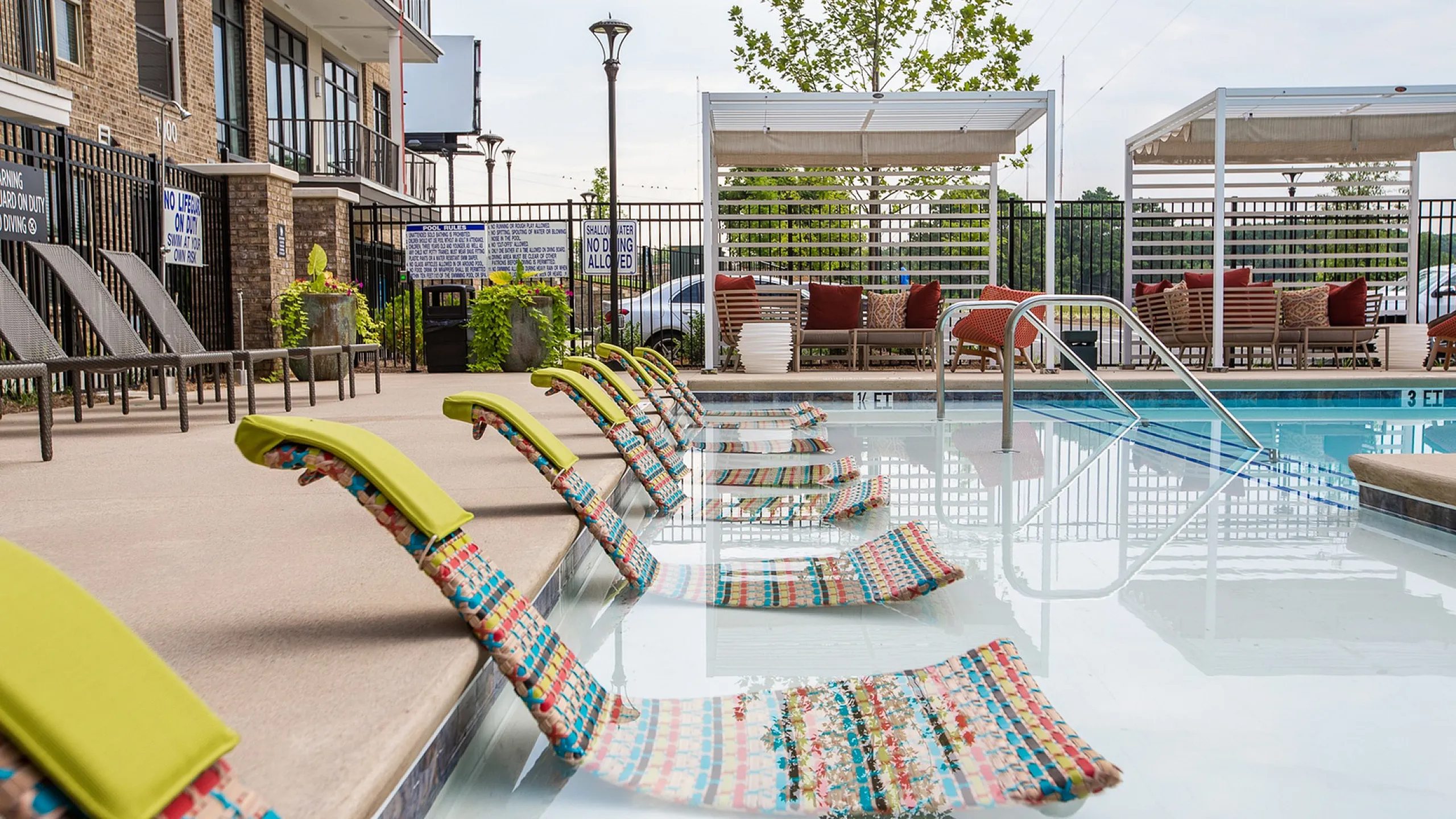 Inviting poolside oasis featuring stylish sun loungers, vibrant decor, and modern cabanas at a luxury apartment complex.
