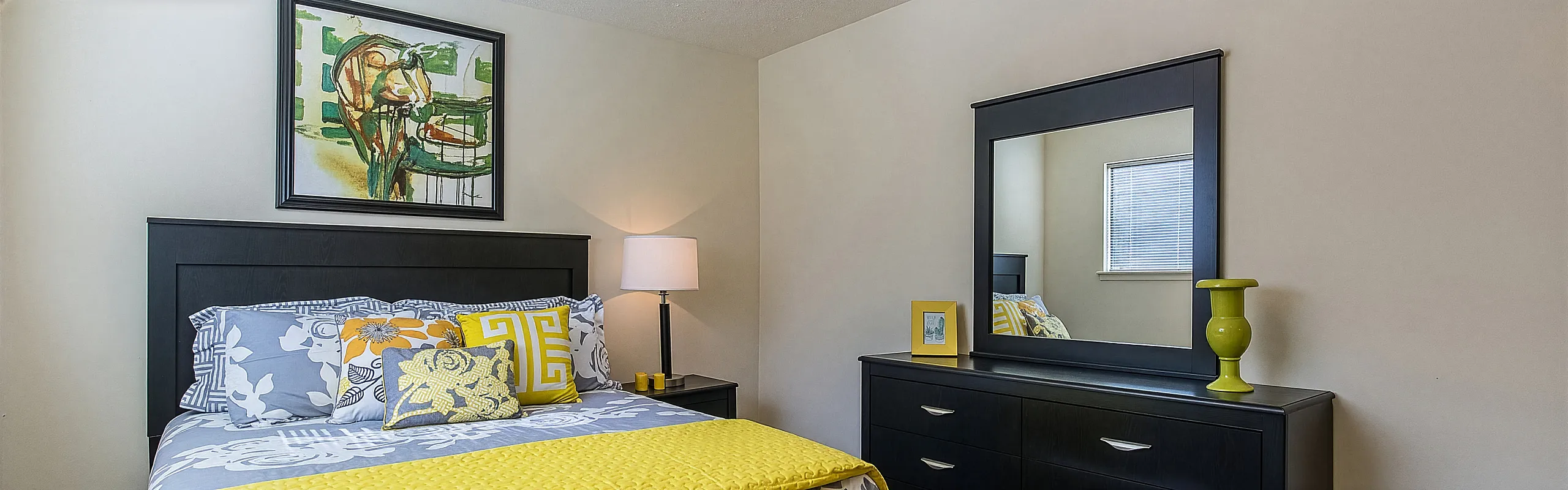 Chic bedroom with elegant modern decor, highlighted by vibrant yellow and grey tones, artistic wall art, and a sleek dresser with mirror.
