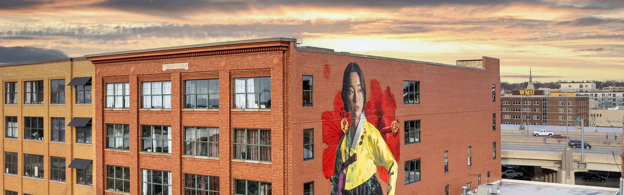 Vibrant urban building with a stunning mural under a picturesque sunset sky, creating an inviting city vibe.