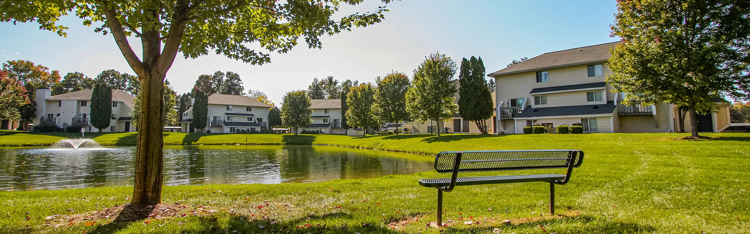 Charming lakeside apartment community with tranquil pond, lush greenery, and inviting outdoor seating.