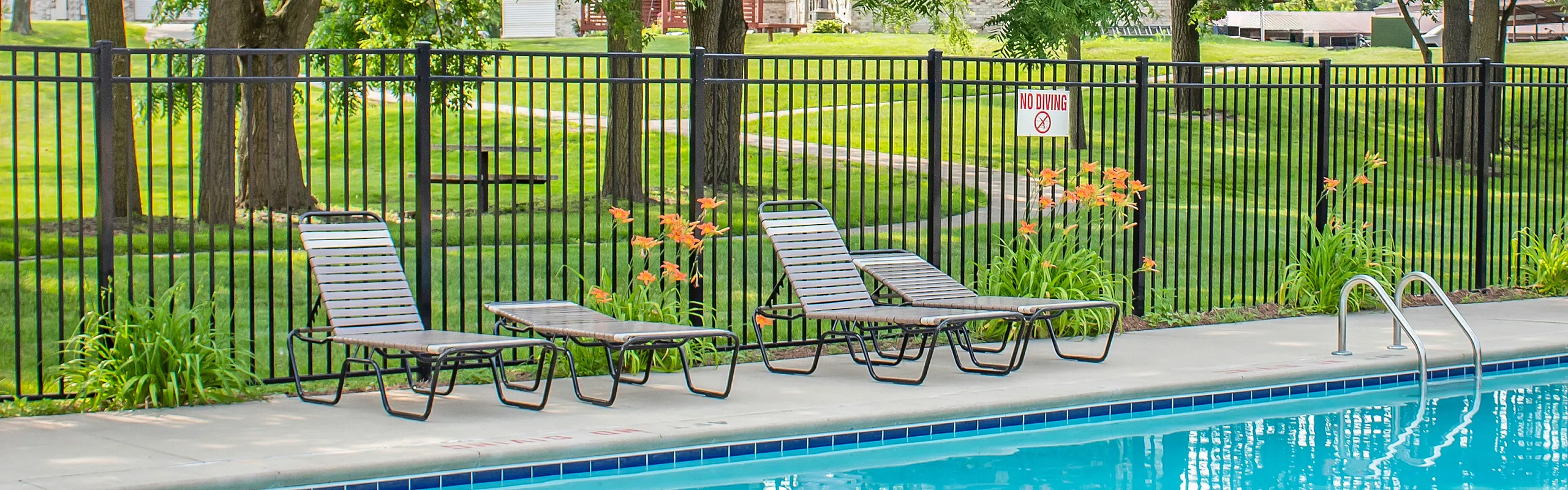 Inviting outdoor pool area with comfortable sun loungers, surrounded by lush greenery and a secure fence, perfect for relaxation.