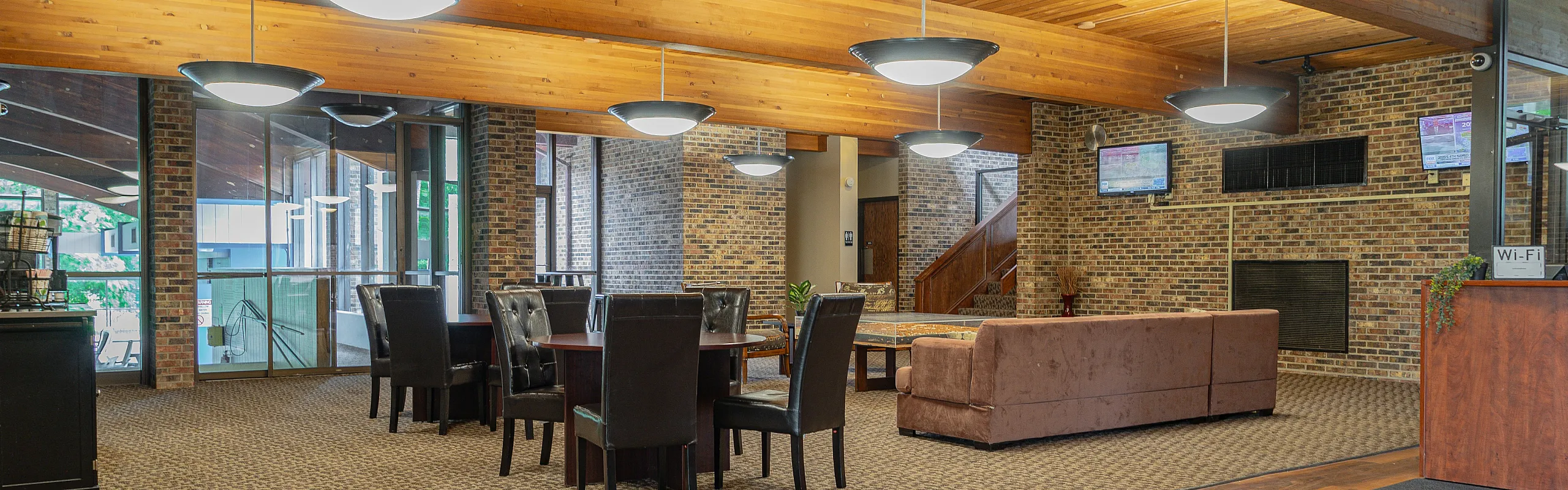 Inviting communal space with chic leather seating, wooden ceilings, and exposed brick walls, offering a cozy and modern ambiance.