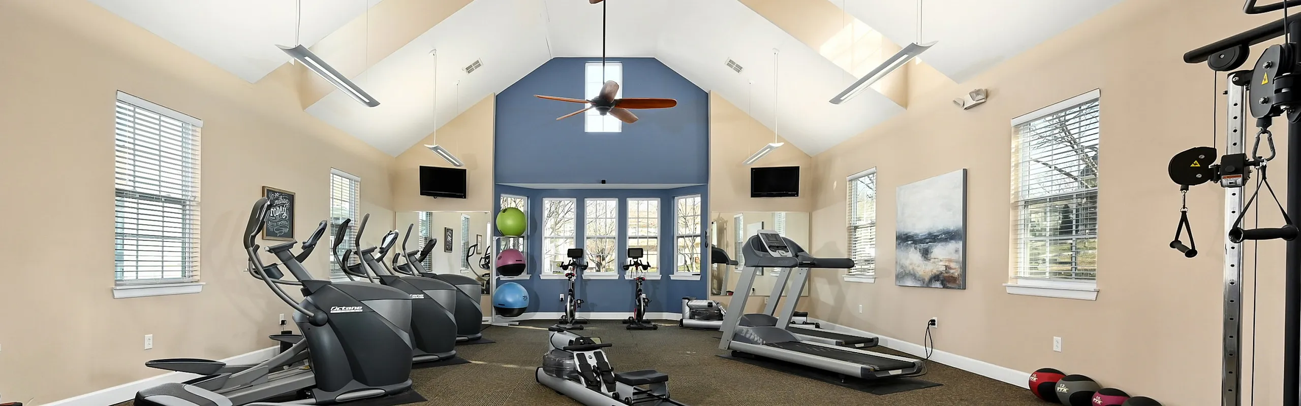 Modern fitness center with state-of-the-art equipment, including treadmills, stationary bikes, and weight machines, under vaulted ceilings with stylish lighting.