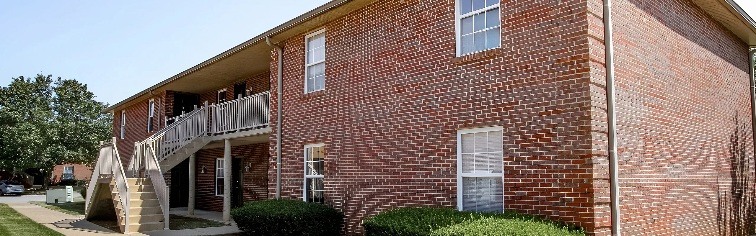 Charming brick apartment exterior with landscaped greenery and inviting staircase entry.