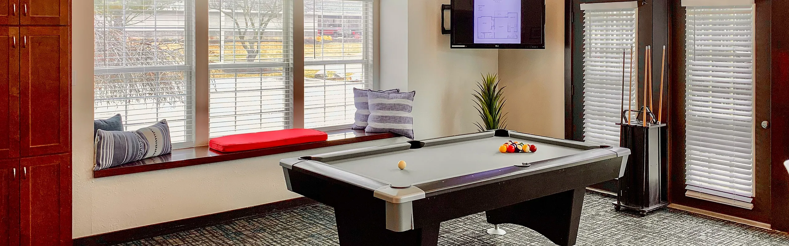 Bright and inviting game room featuring a sleek billiards table, large windows with cozy seating, and stylish decor.
