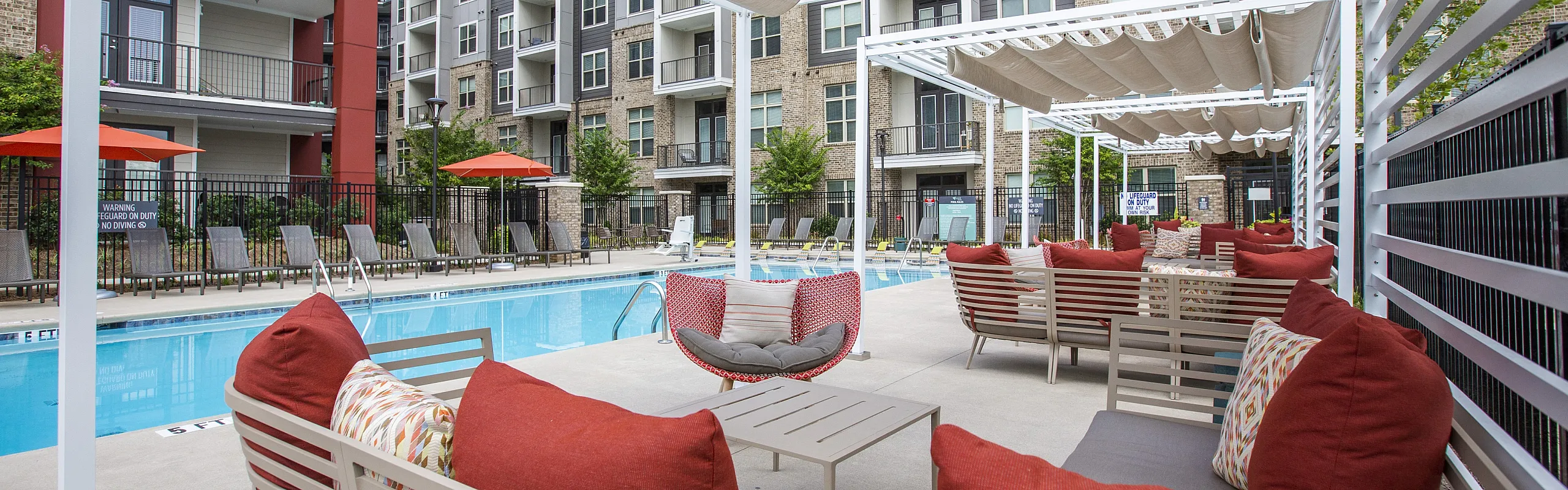 Luxurious apartment complex with a sparkling pool, modern lounge area, and vibrant outdoor seating.