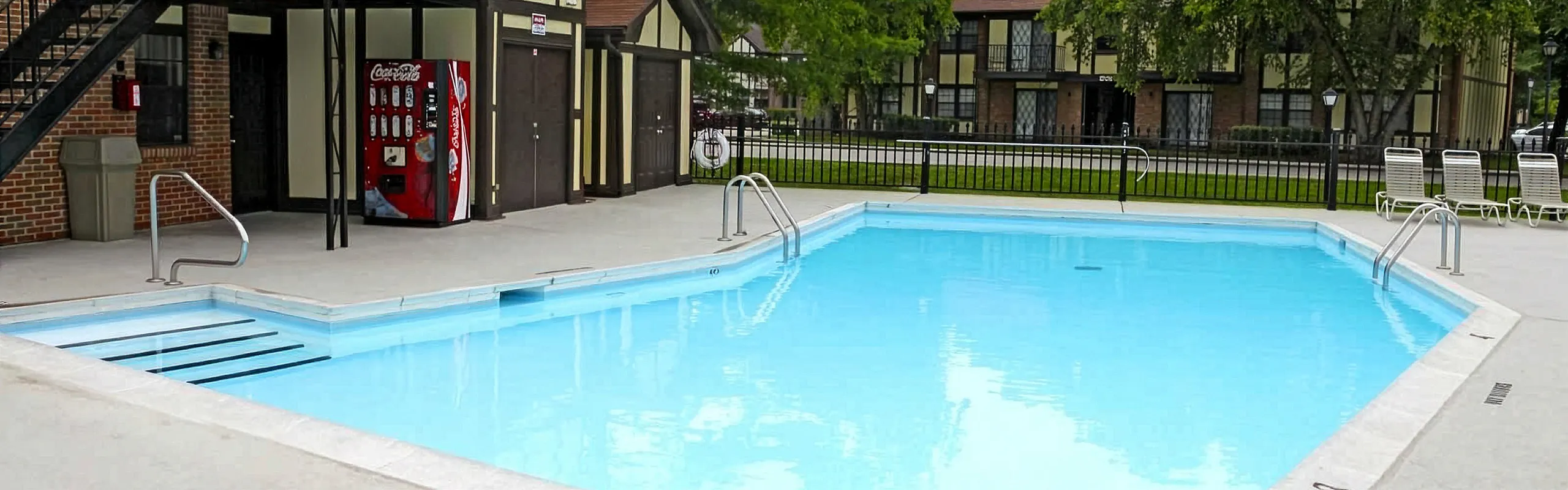 Inviting outdoor swimming pool area with lounge chairs and a classic brick building backdrop, perfect for relaxation and enjoyment.