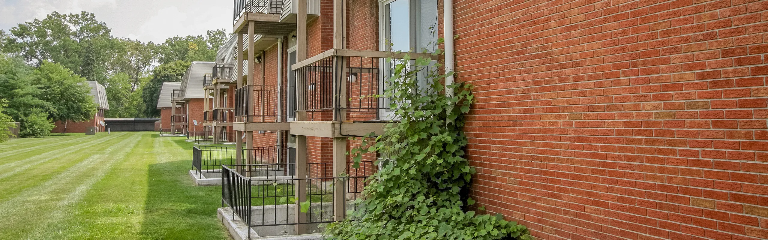 Charming brick apartment building with private balconies and lush green surroundings.