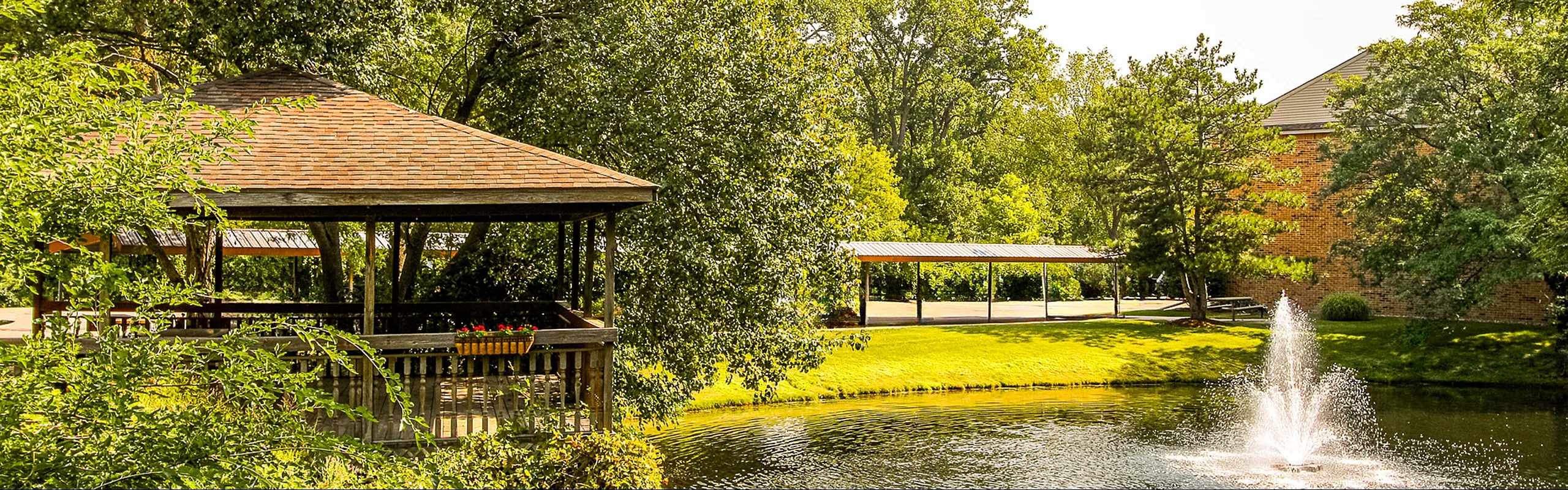 Charming outdoor area with a rustic gazebo overlooking a serene pond and elegant fountain, surrounded by lush greenery and a peaceful atmosphere.