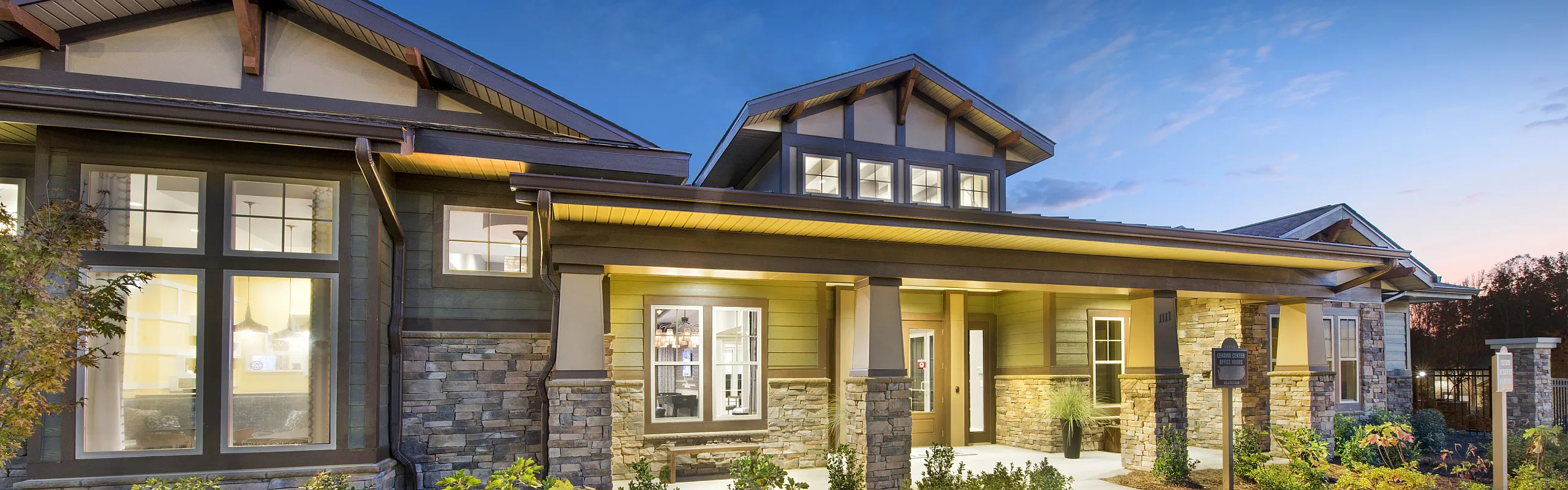 Charming suburban house exterior at dusk with warm lighting, stone accents, and beautifully landscaped entrance.