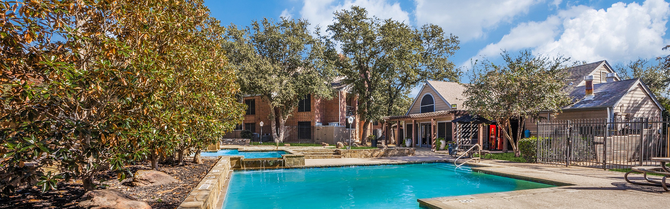 Charming apartment complex with a serene outdoor pool surrounded by lush greenery and elegant architecture.