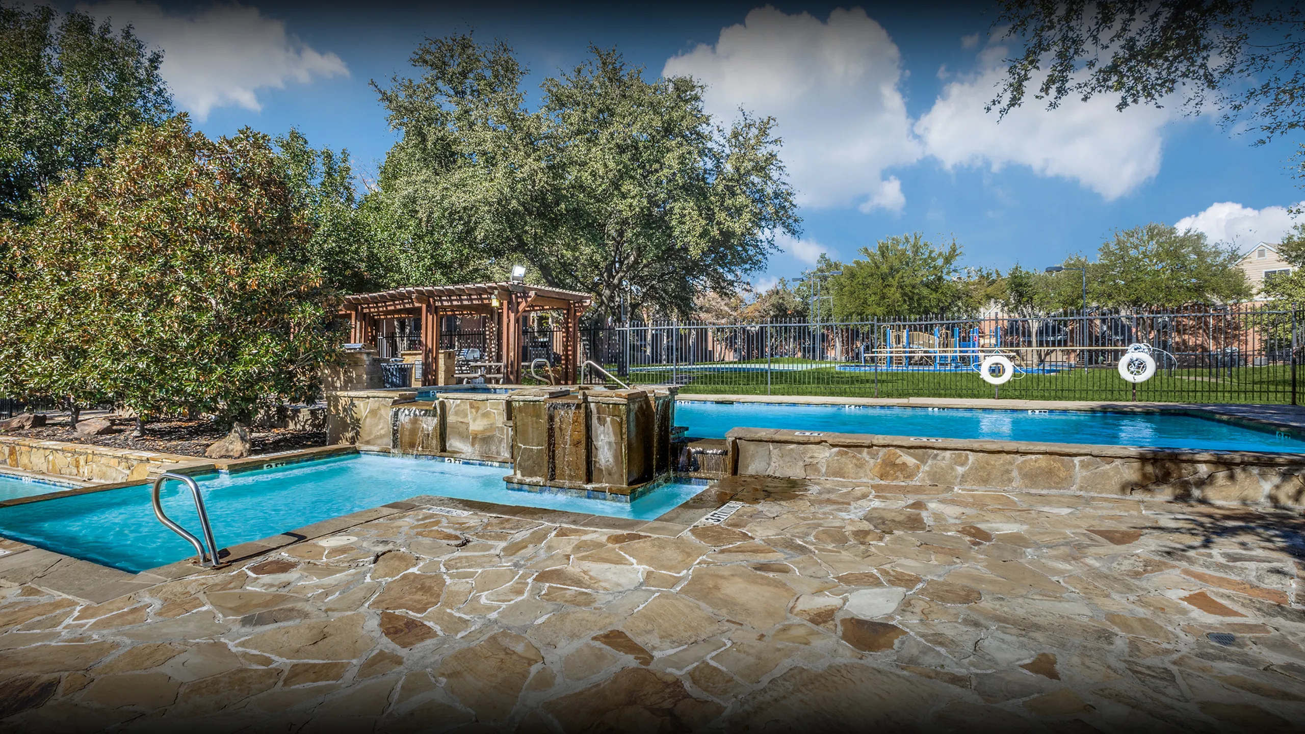 Inviting outdoor pool area featuring a serene waterfall, lush greenery, and a charming pergola, perfect for relaxation.
