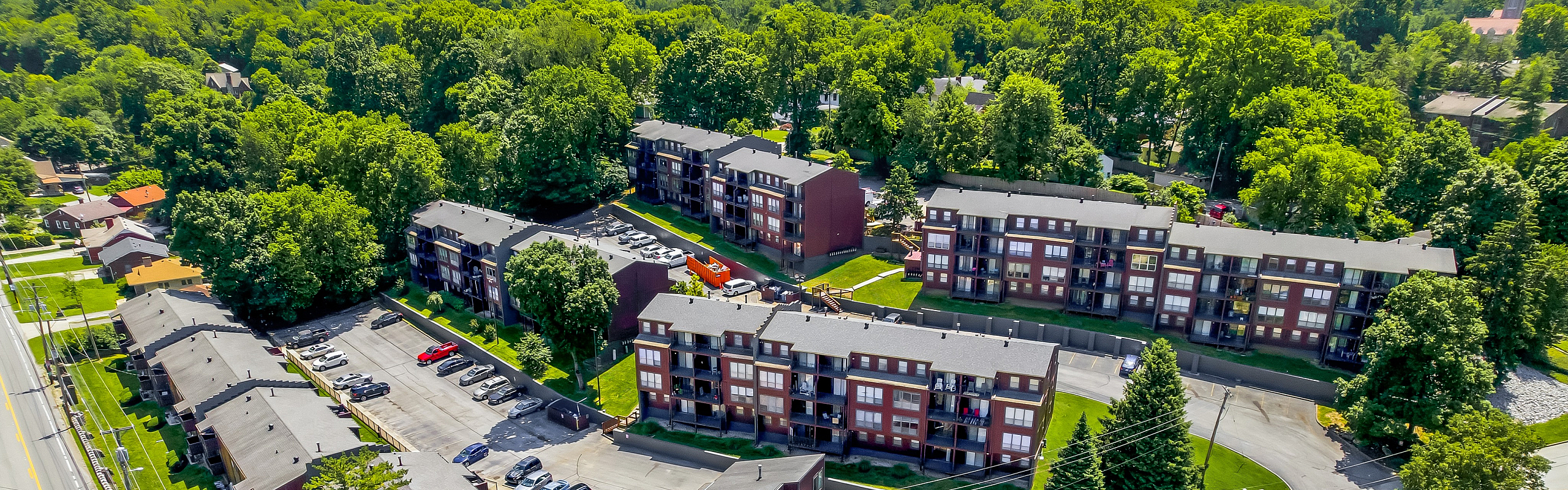 Charming aerial view of a lush, green apartment complex surrounded by vibrant forests and well-maintained landscaping.