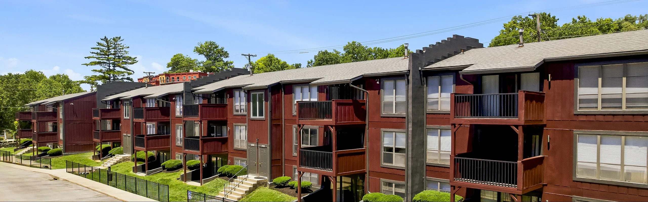 Charming red-brick apartment complex with lush greenery and modern balconies under a clear blue sky.