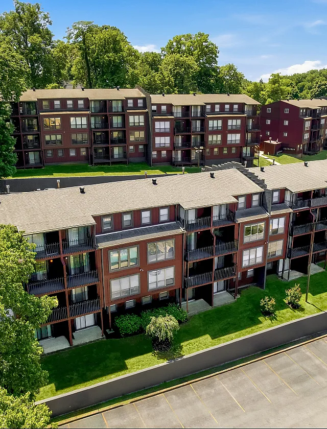 Charming apartment complex surrounded by lush greenery, featuring multiple balconies and ample parking space.