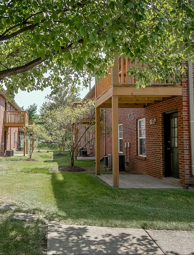 Charming exterior view of brick apartments with private balconies, surrounded by lush greenery and tranquil pathways.