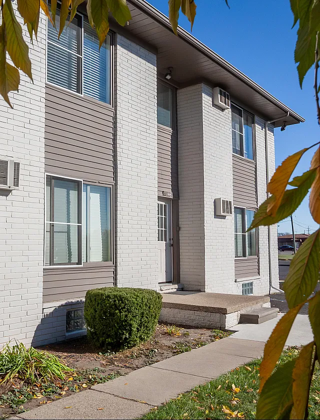 Charming apartment building with a modern brick facade, lush landscaping, and clear blue skies, perfect for comfortable living.