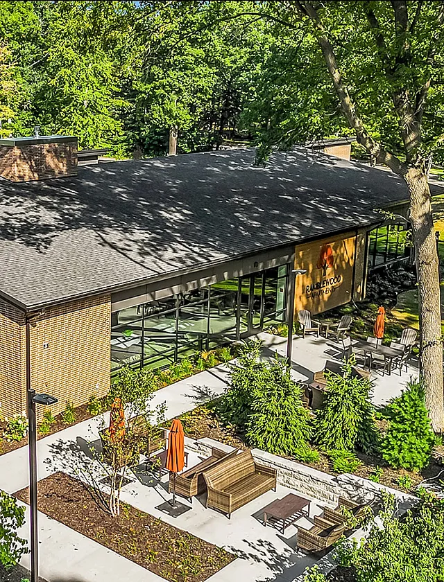 Aerial view of a modern apartment complex surrounded by lush greenery, featuring outdoor seating and vibrant landscaping.