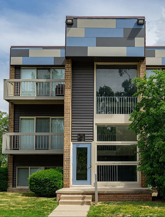 Contemporary apartment building featuring modern architecture with large windows and private balconies surrounded by lush greenery.