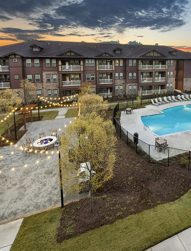 Charming apartment complex with a beautifully lit outdoor space, featuring a sparkling swimming pool and cozy fire pit area at sunset.