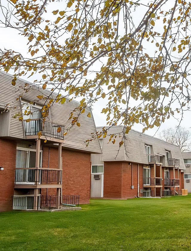Charming apartment complex with modern balconies and lush green lawns, nestled under a canopy of fall leaves.