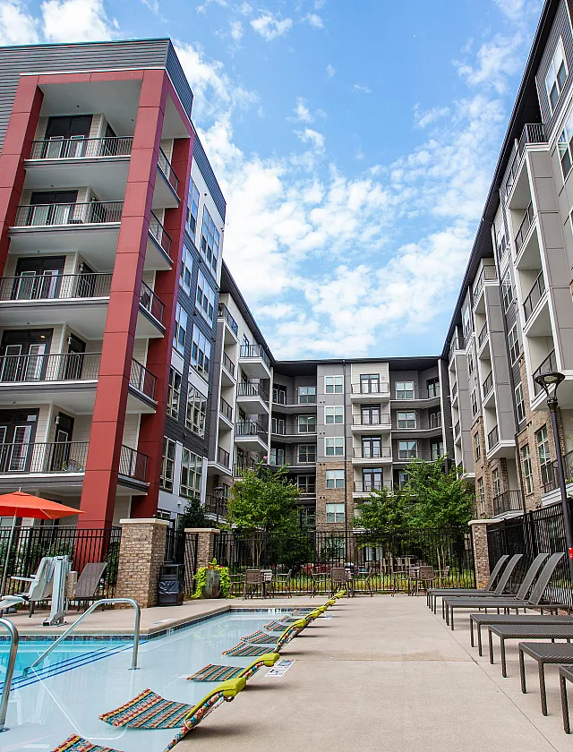 Modern apartment building with elegant balconies surrounding a luxurious pool and stylish patio area, perfect for relaxation and entertainment.