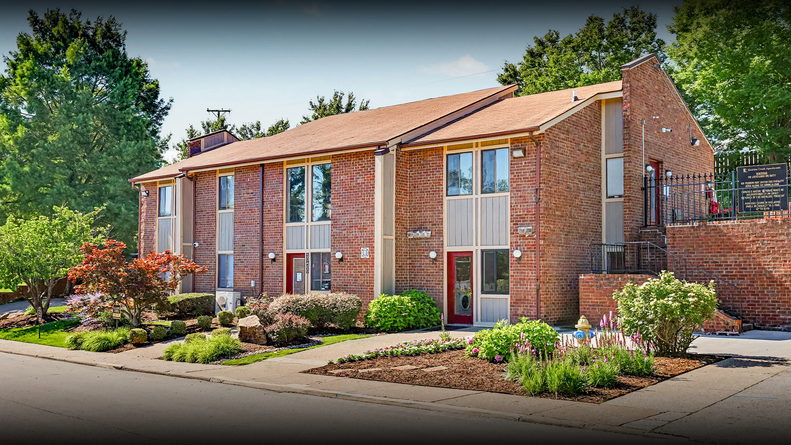 Charming brick apartment building with lush landscaping and vibrant flowers, offering an inviting and comfortable living environment.
