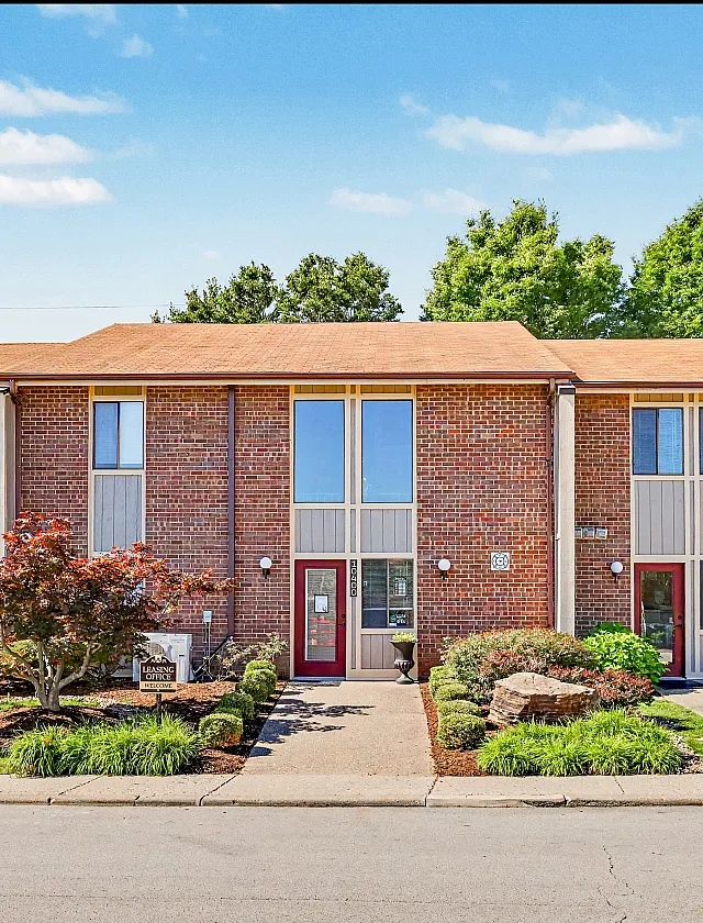 Charming brick townhouse with modern double windows and lush landscaping, featuring a welcoming entrance.