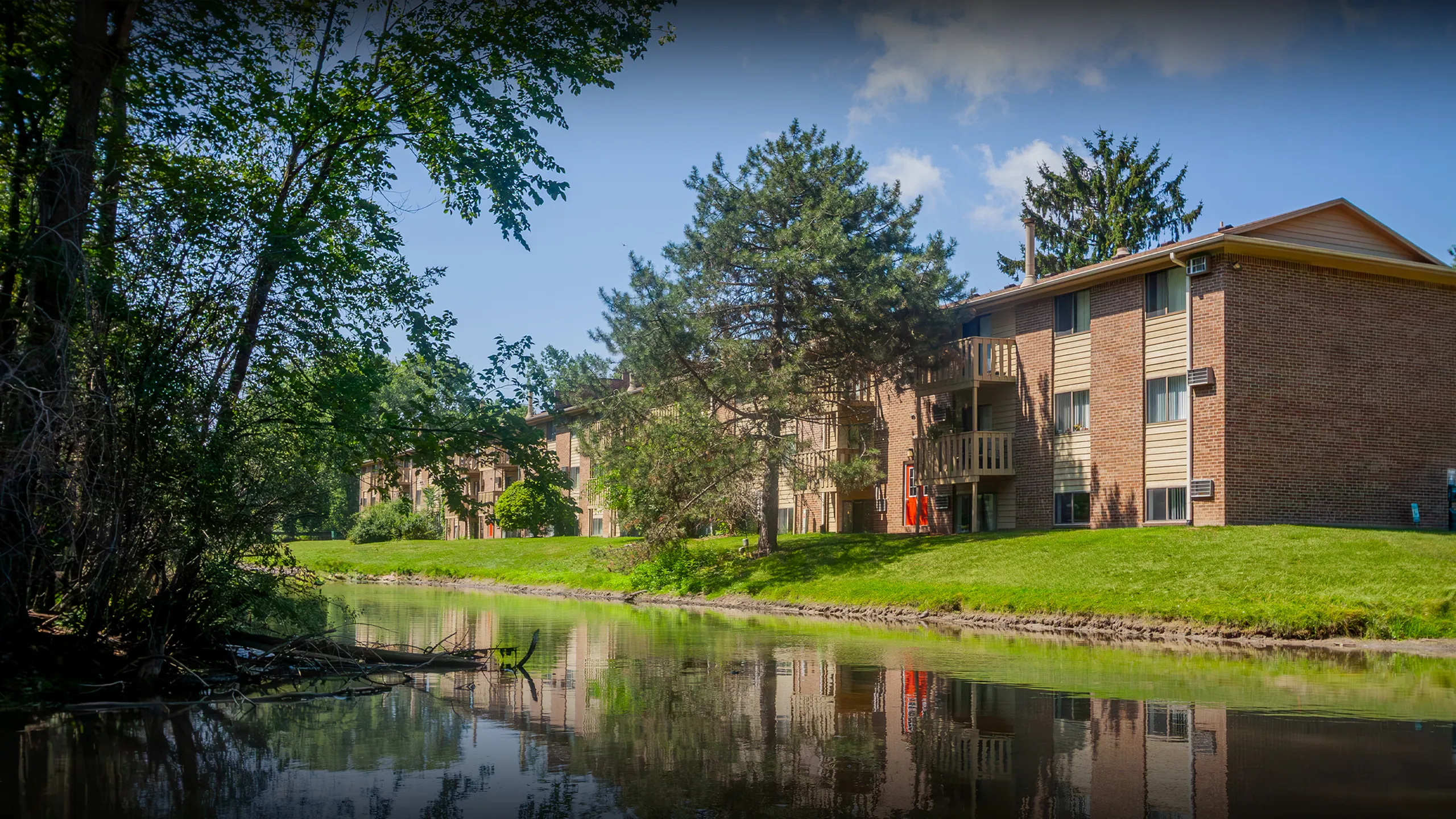Serene apartment complex surrounded by lush greenery and a tranquil pond, offering a peaceful living environment.