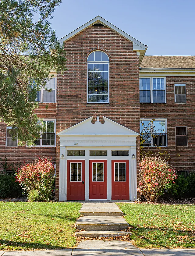 Charming brick apartment building with eye-catching red doors and lush landscaping, offering a welcoming entry.