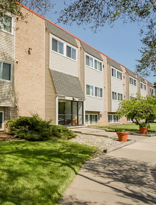 Charming brick apartment building with manicured lawns and inviting entrance, surrounded by lush greenery.