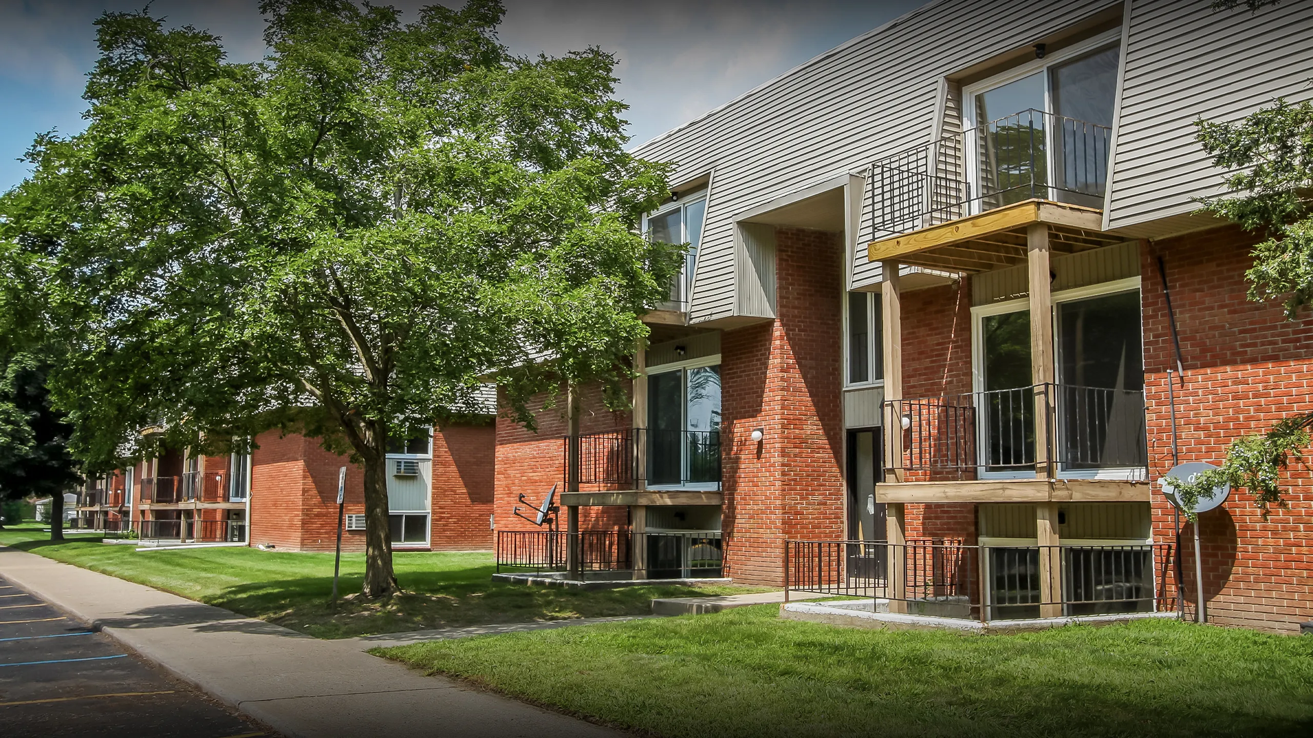Charming red-brick apartment complex with private balconies and lush green surroundings, ideal for comfortable living.