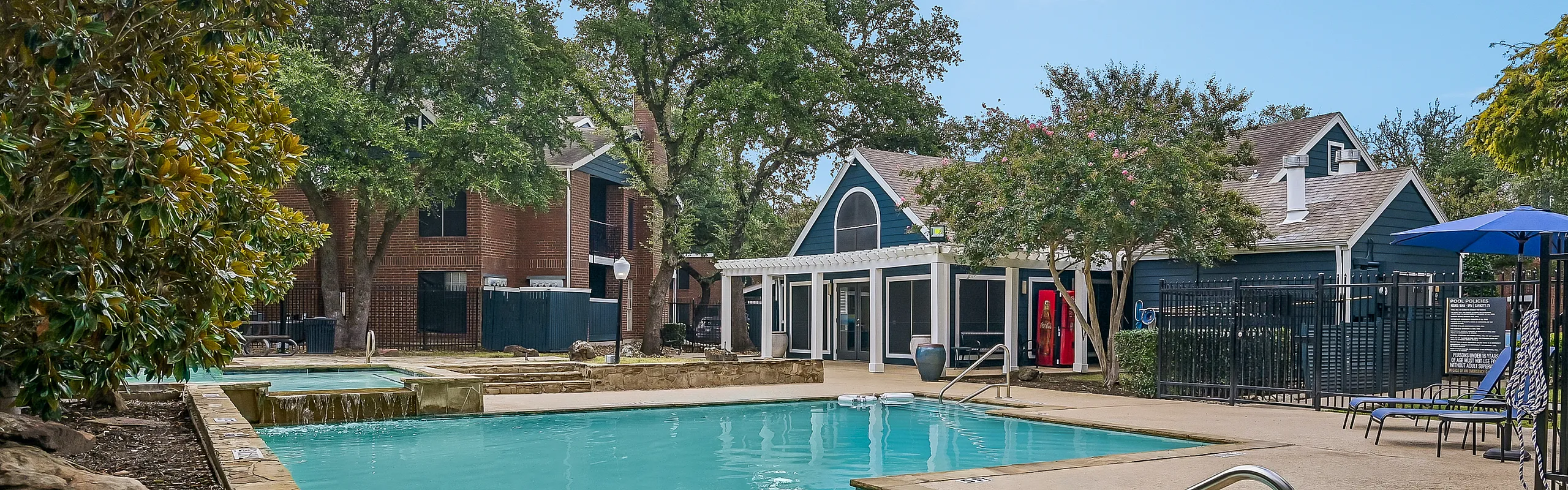 Inviting apartment complex featuring a refreshing swimming pool, lush greenery, and charming architectural design.