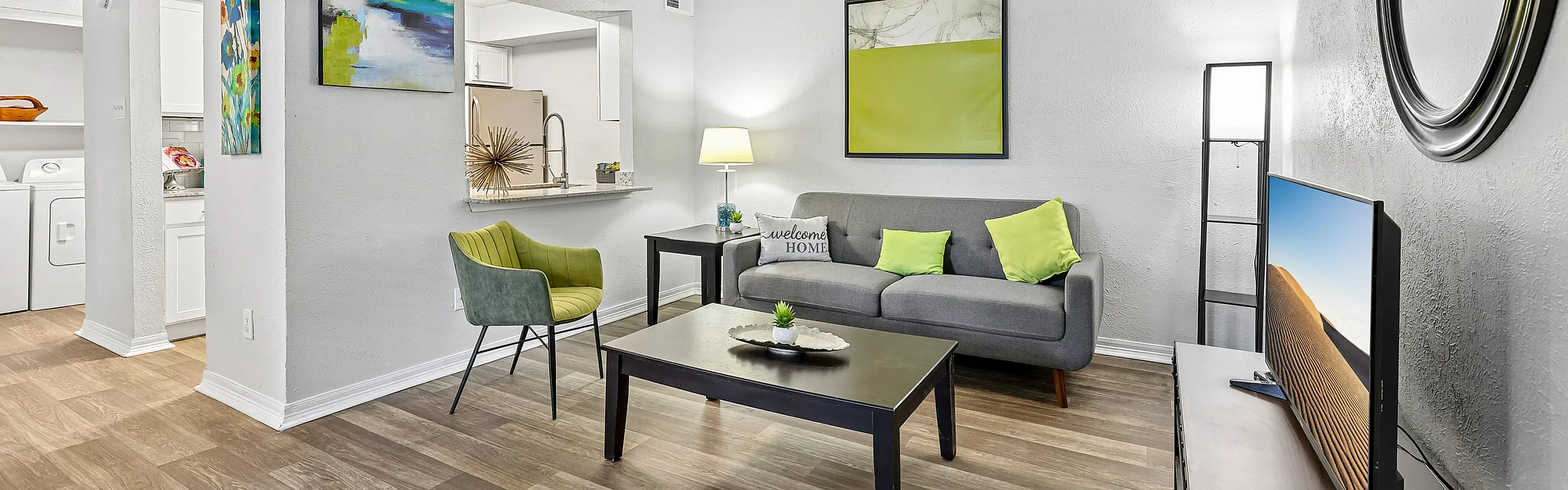 Inviting living room with modern decor, vibrant artwork, and cozy seating adjacent to a functional kitchen and laundry area.