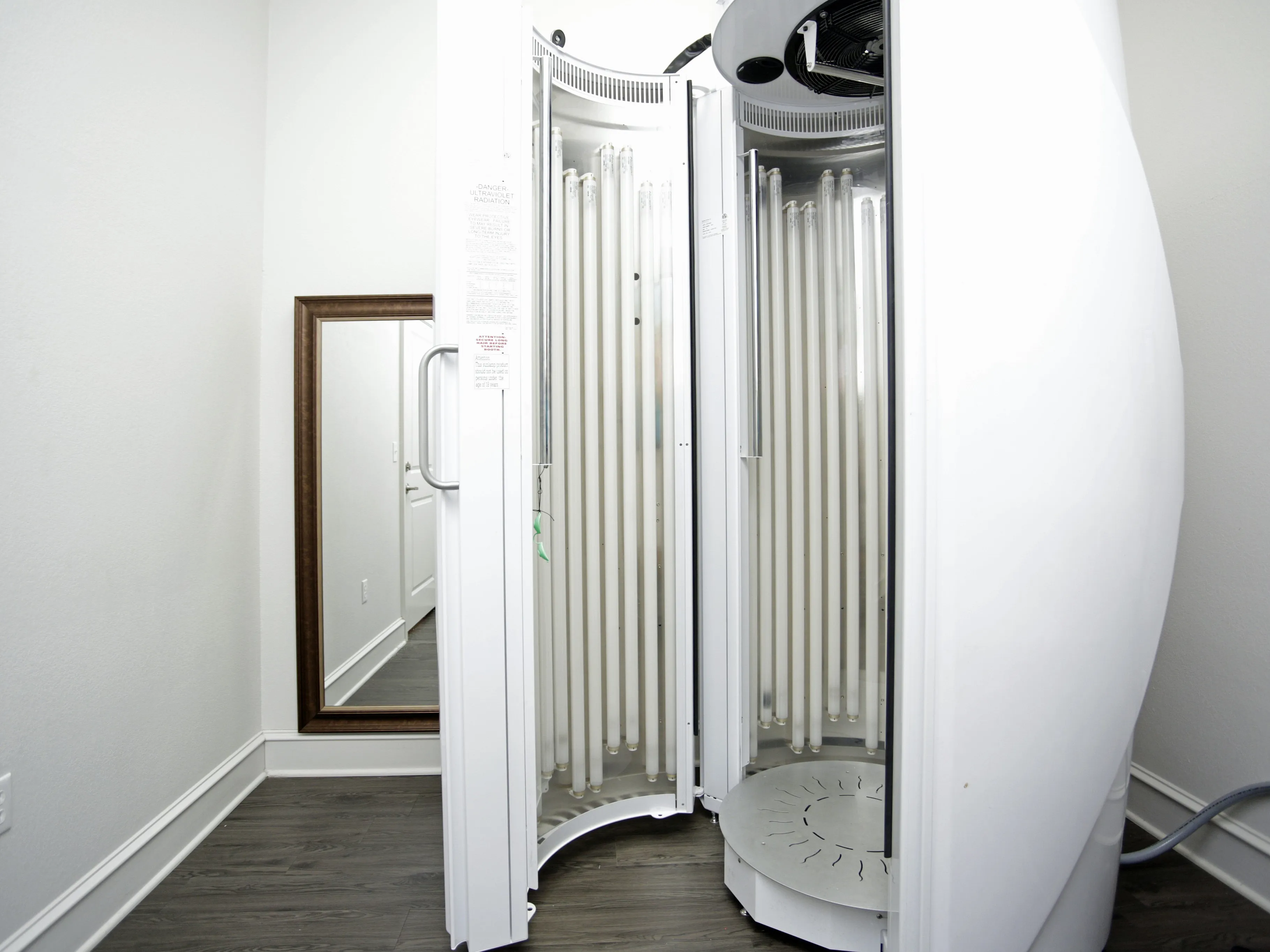 Modern tanning booth in a cozy corner with a stylish floor-length mirror and elegant dark wood flooring.