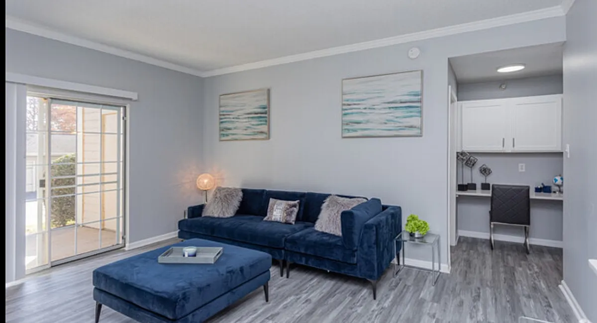 Modern living room featuring a plush navy sofa, stylish artwork, and a cozy workspace, bathed in natural light from large sliding doors.