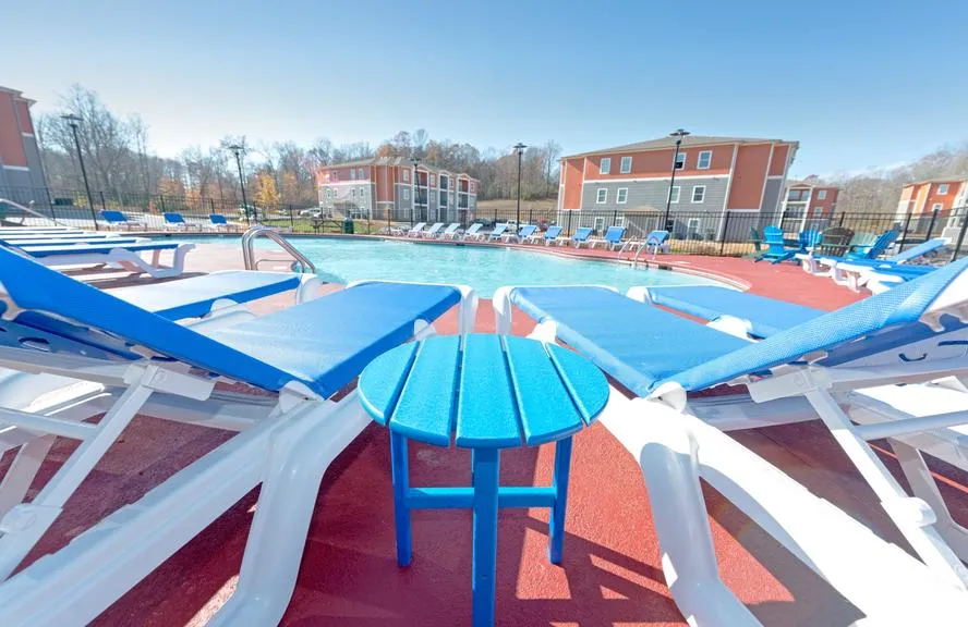 Inviting poolside view with comfortable blue lounge chairs, perfect for relaxation, surrounded by modern apartment buildings and serene natural scenery.