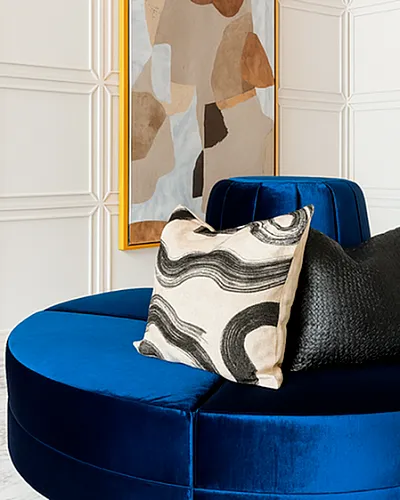 Chic interior featuring a luxurious blue velvet round sofa with contemporary abstract art and stylish pillows.