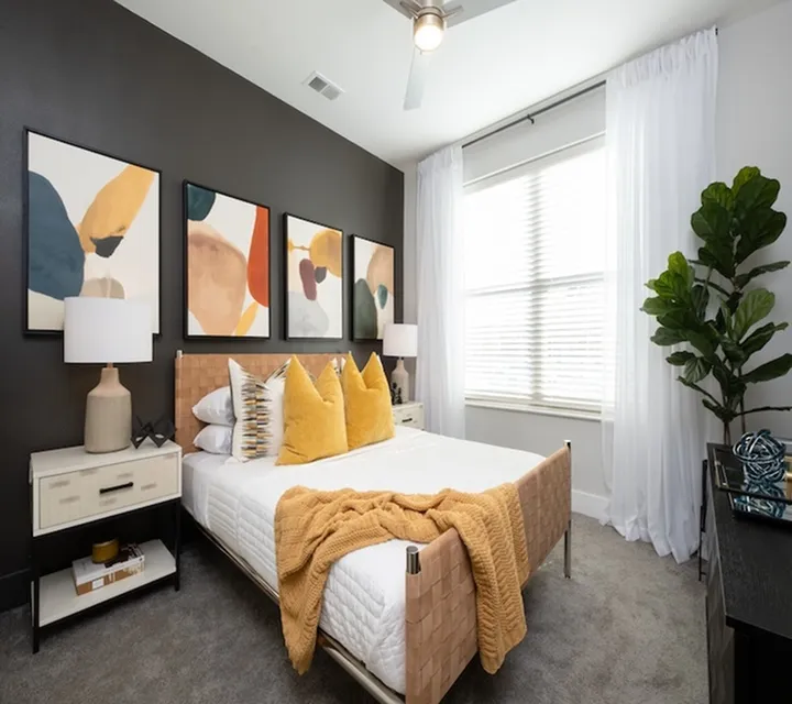 Stylish bedroom with modern decor, featuring abstract artwork, a cozy bed with vibrant pillows, and natural light from large windows.
